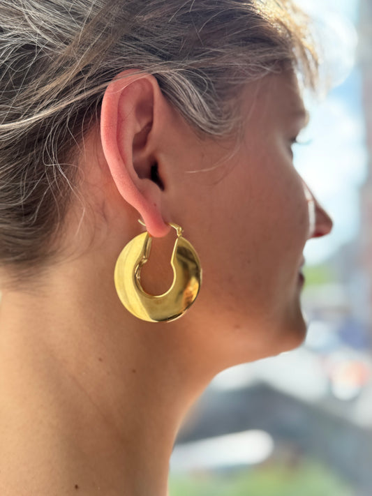 Gold hoop earring worn by a person with a blurred outdoor background