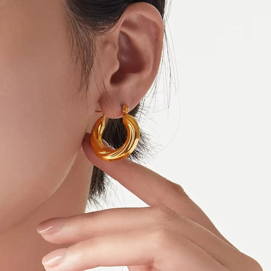 Gold hoop earring worn by a person on a plain background