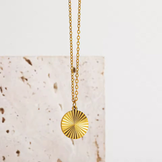 Gold necklace with a sunburst pendant on a light background
