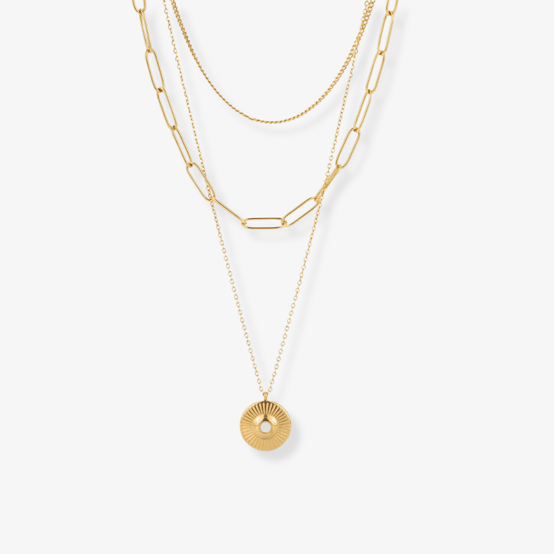 Three necklaces layered at different lengths with mixed chain textures and a round pendant