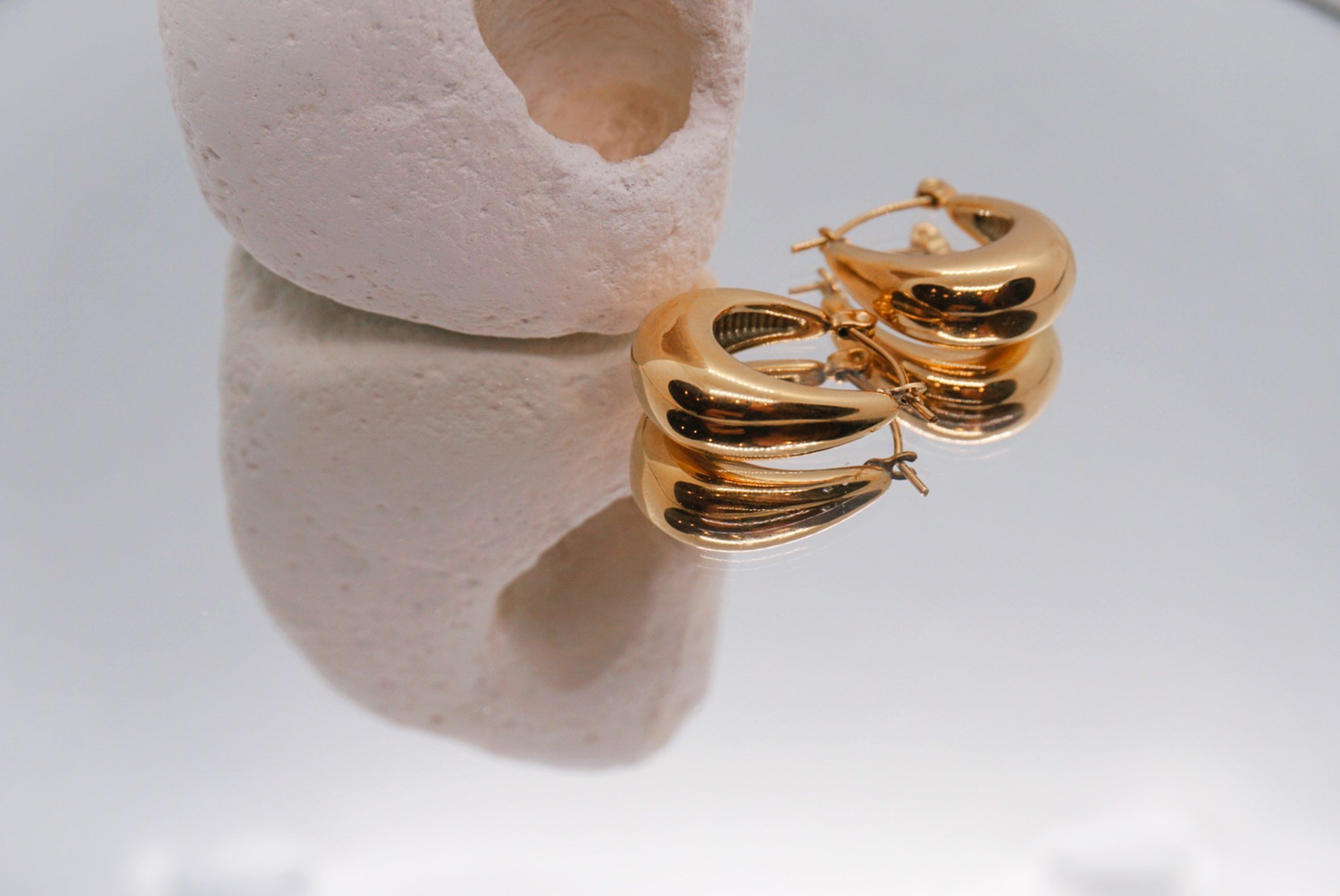 Luzza Studio gold earrings collection – sculpted hoops stacked on ceramic backdrop