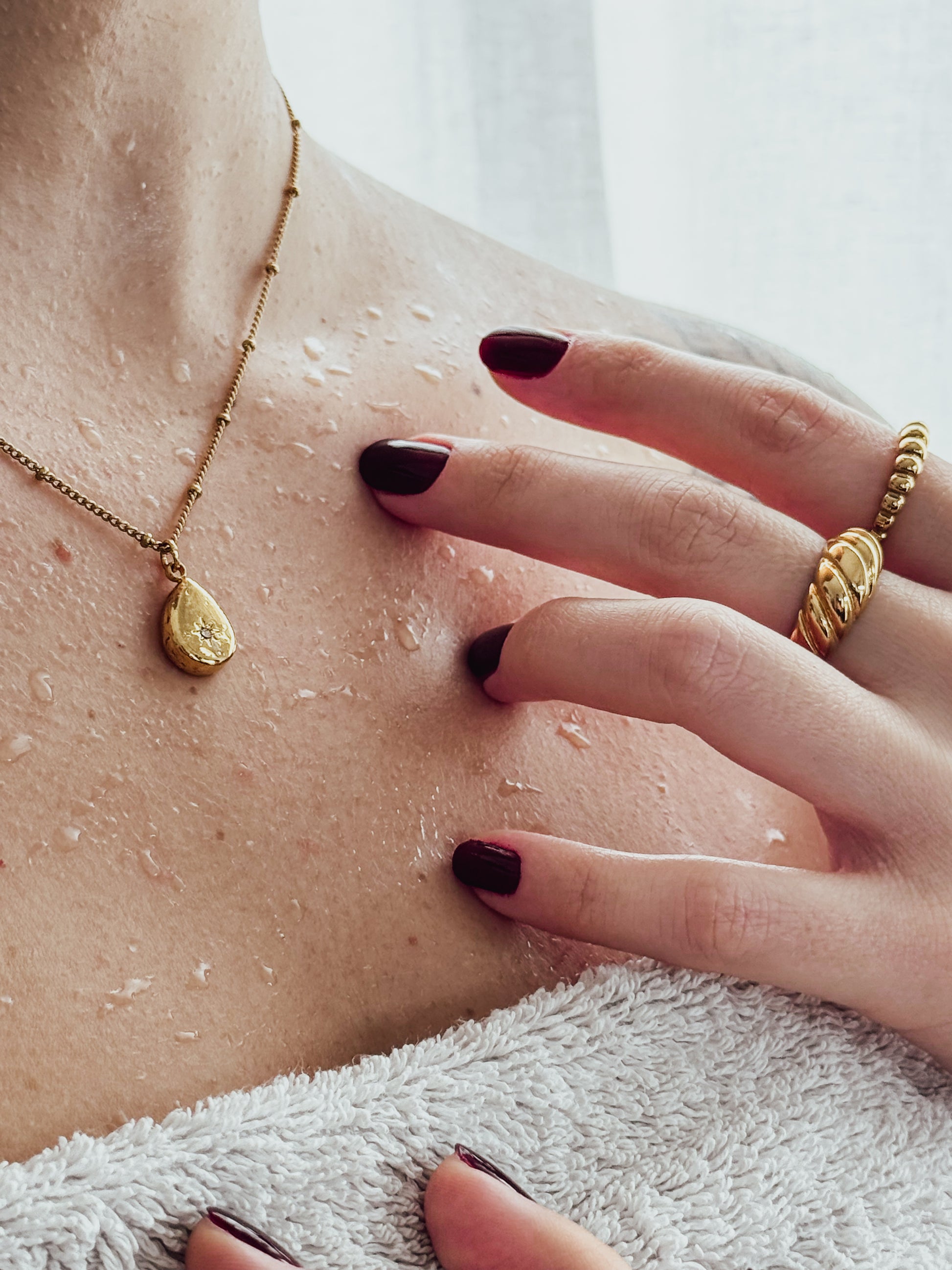 Close-up of a person's hand with a gold ring and necklace, touching their skin.