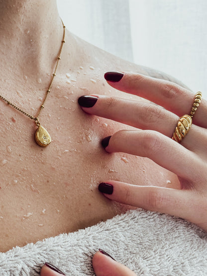 Close-up of a person's hand with a gold ring and necklace, touching their skin.