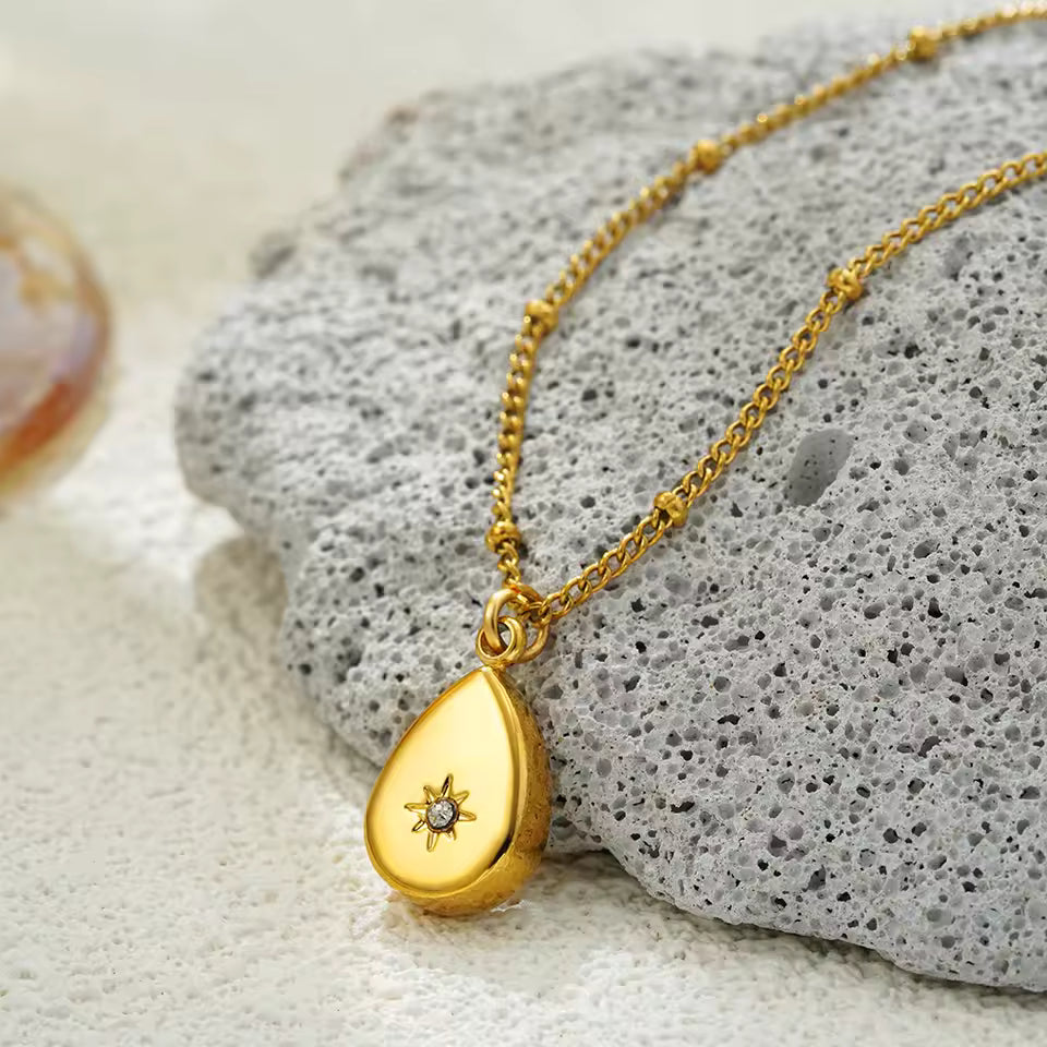 Gold necklace with a teardrop-shaped pendant on a textured stone surface
