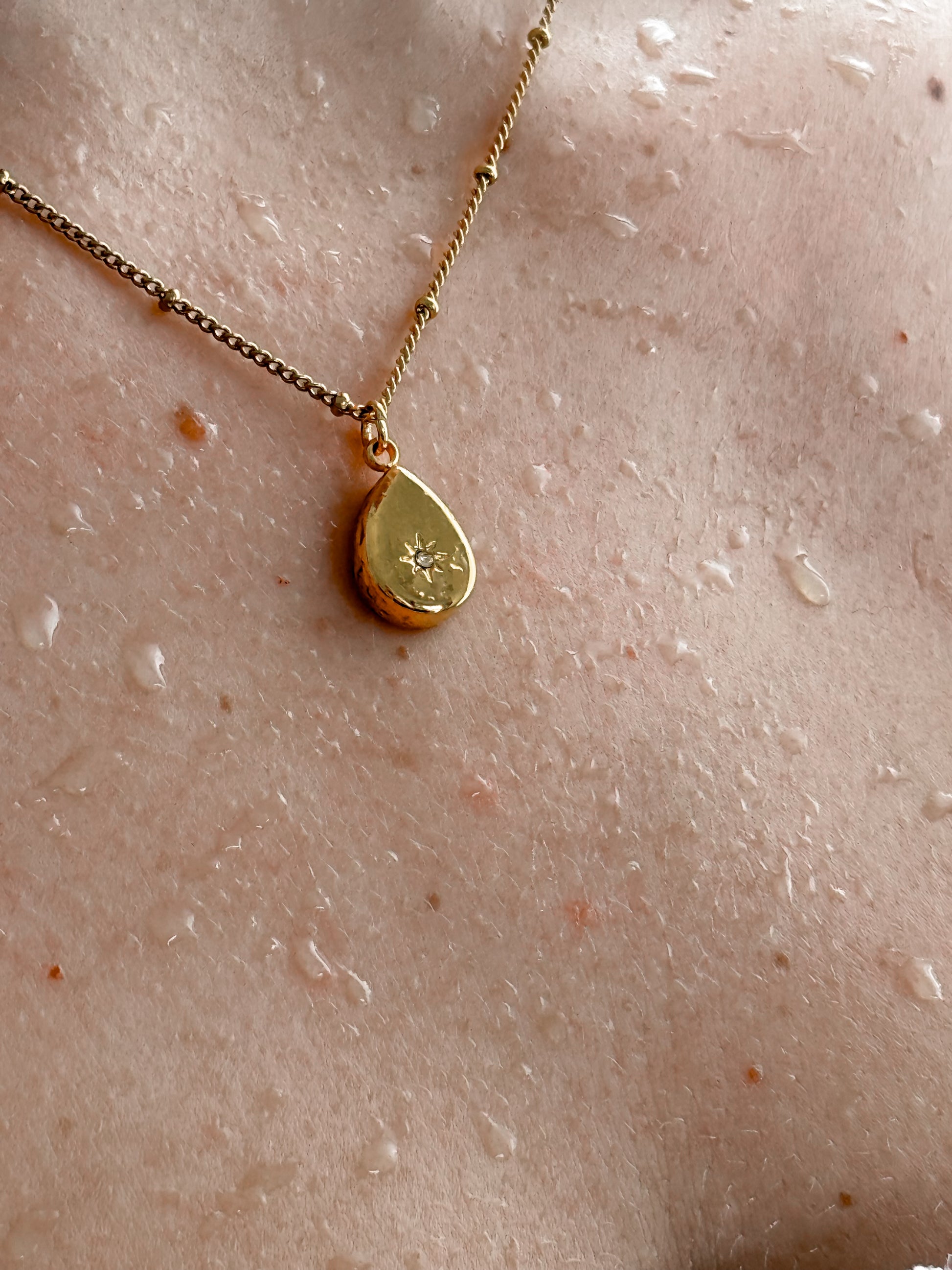 Gold necklace with a teardrop pendant on a textured beige surface