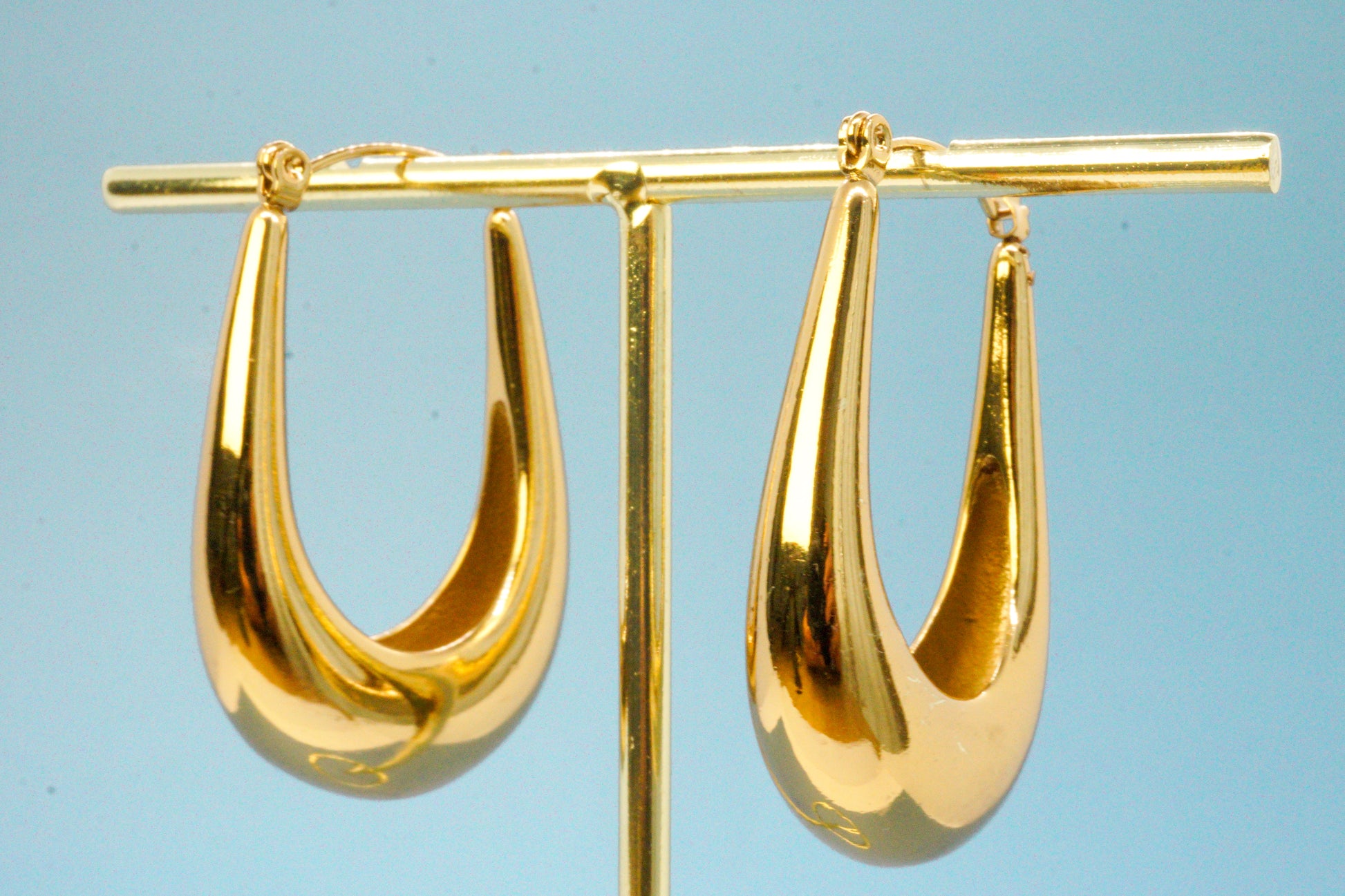 Élan Earrings – Gold teardrop earrings on blue backdrop, minimal product shot by Luzza Studio	