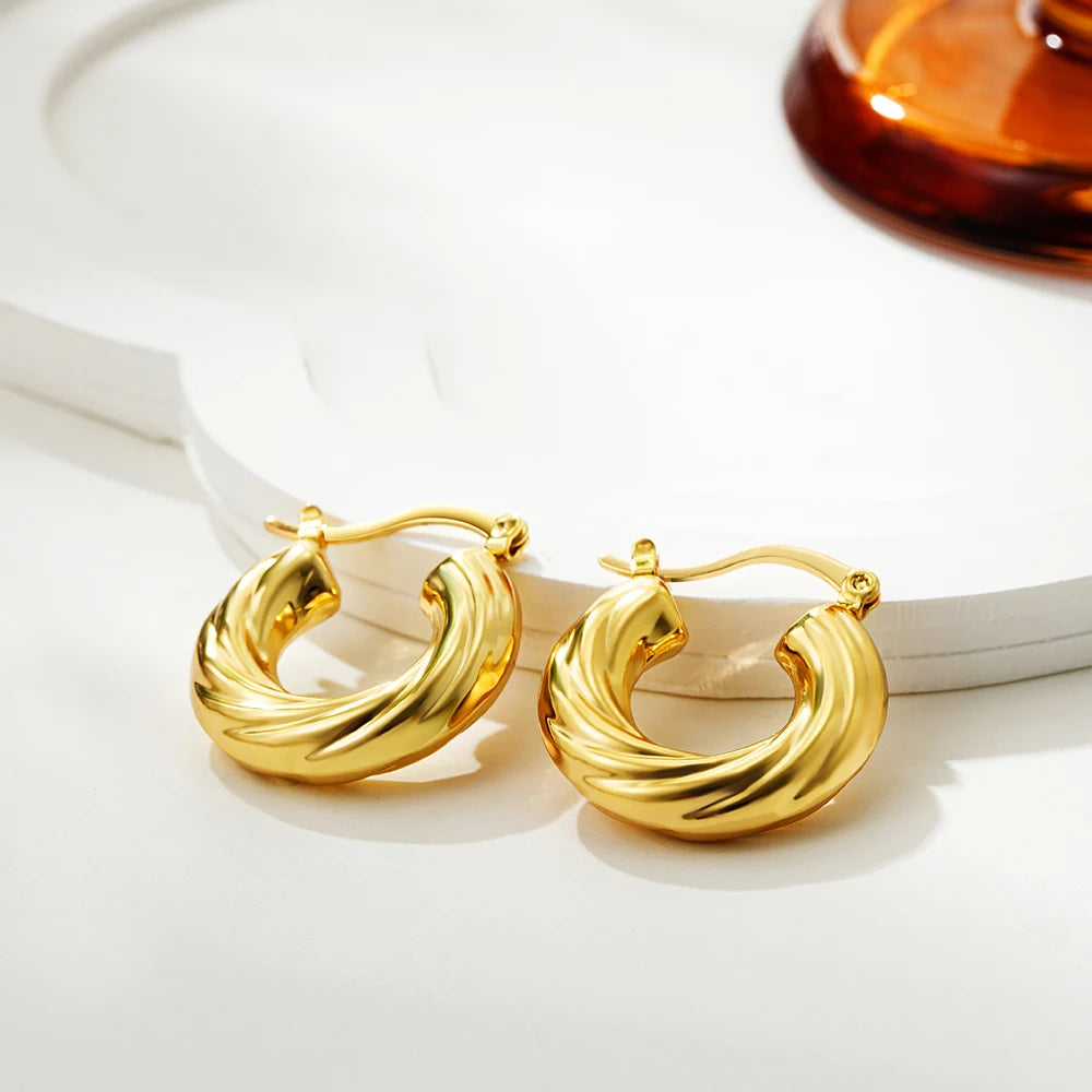 Gold hoop earrings on a white surface with a blurred background